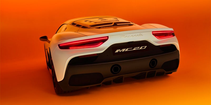 Rear view of a white Maserati MC20 sports car with illuminated red taillights and black accents against an orange background.