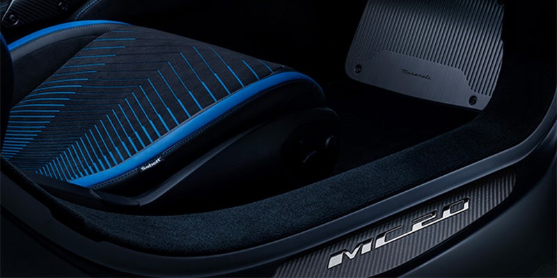 A Maserati car interior with a black seat accented with blue lines and trim, and an 'MC20' badge on the door sill.