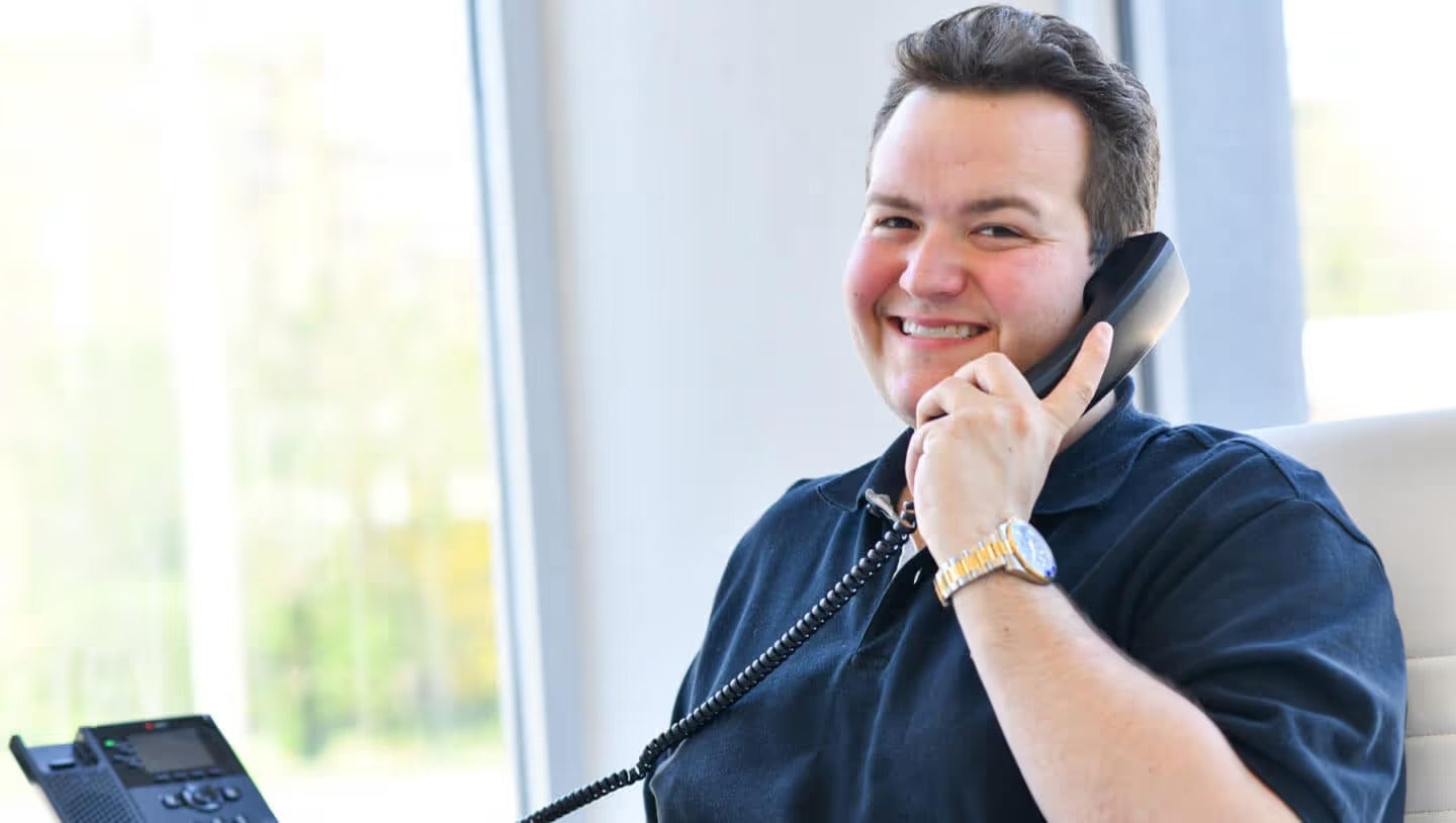 Cody Yager sales specialist answers a corded desk phone, looking friendly.